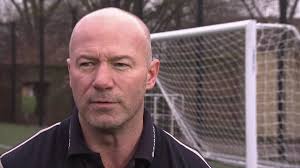 A serious Alan Shearer standing in front of a goal.